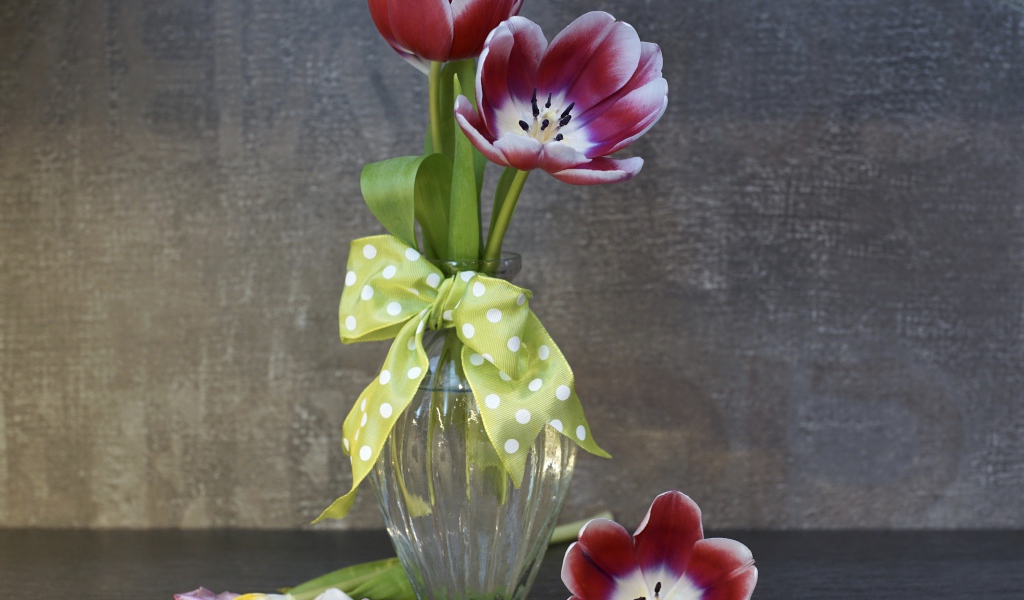 Три розовых цветка тюльпана в стеклянной вазе у стены