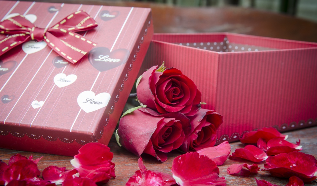 Три красные розы с лепестками  на столе с подарком