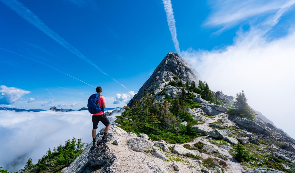 Мужчина подымается на вершина горы под голубым небом 
