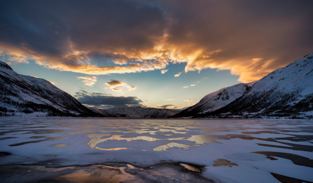 Покрытое льдом озеро у гор на закате солнца 