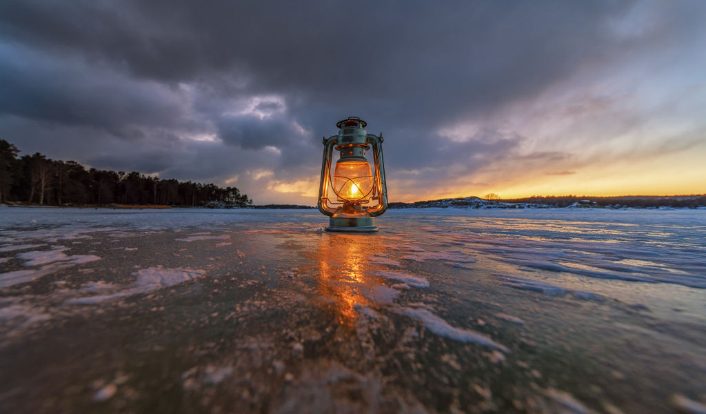 A kerosene lamp stands on the ice-covered shore