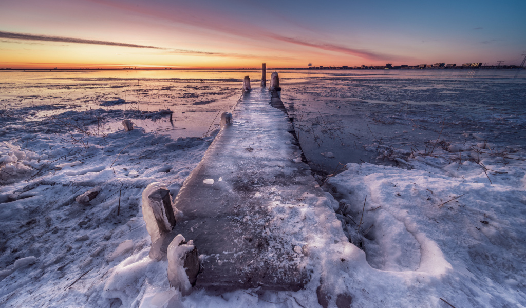 Покрытый льдом деревянный мост у озера 