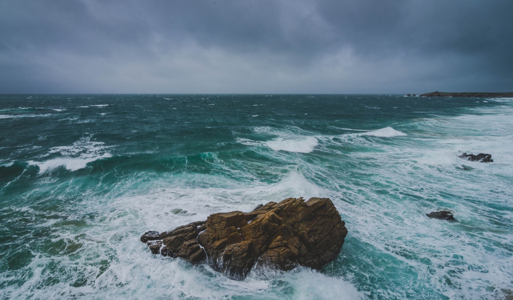 Большой камень омывают белые волны океана 