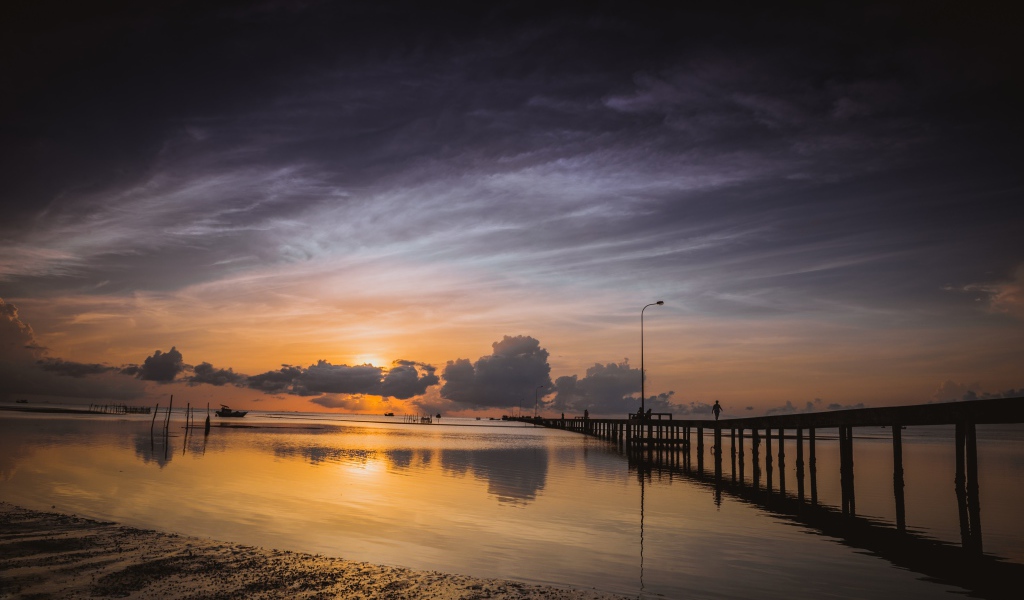 Деревянный мост на реке в лучах  солнца на закате