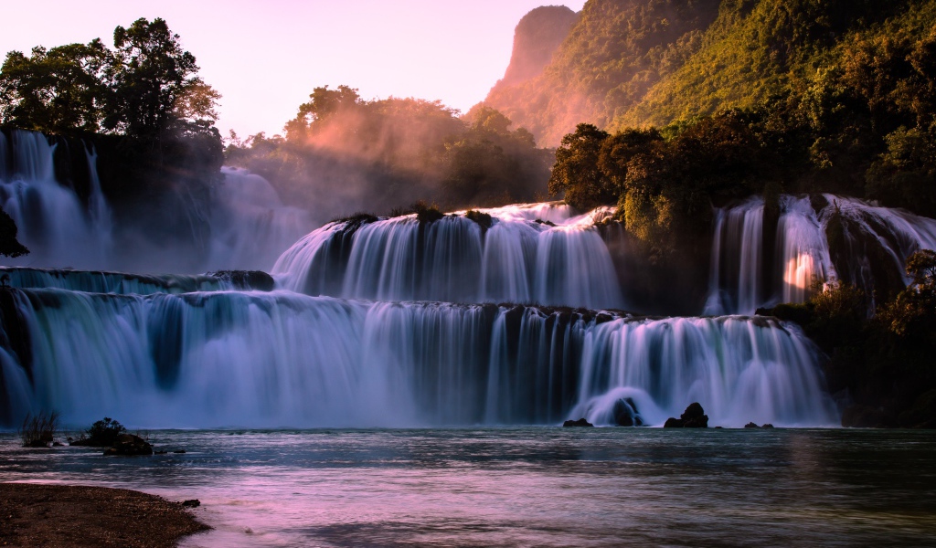 Каскадный водопад стекает по камням в лучах солнца 