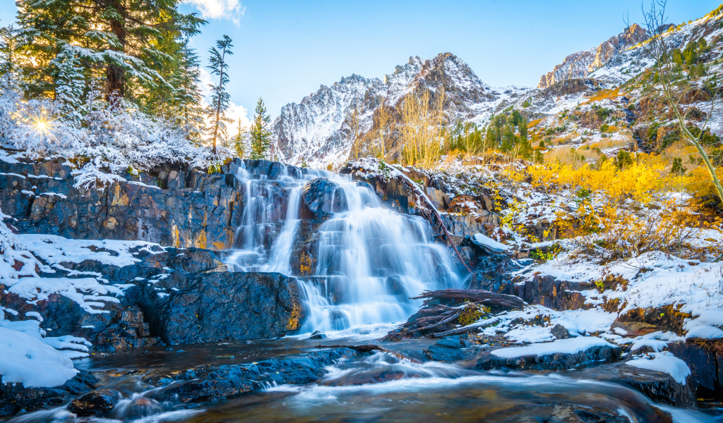 Водопад стекает по покрытым снегом камнях в горах