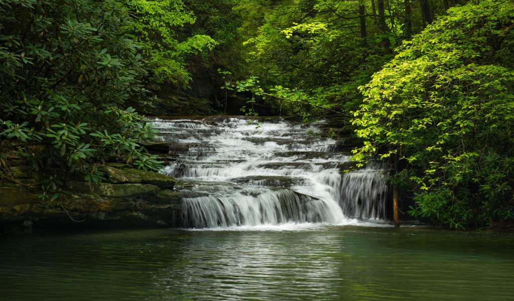 Водопад стекает по каменному каскаду в реку 