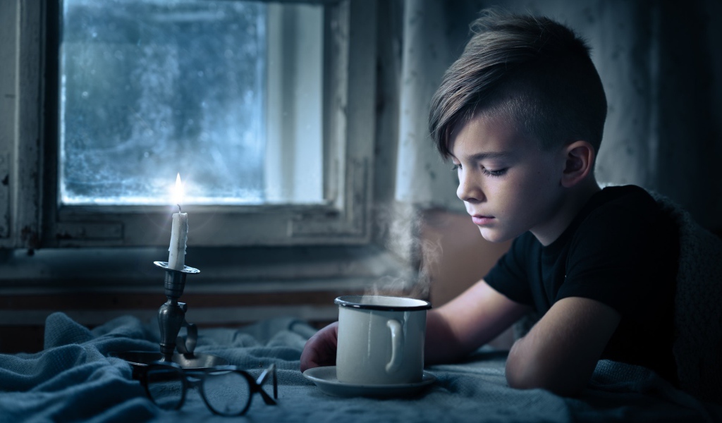 Маленький мальчик сидит за столом при свете свечи 