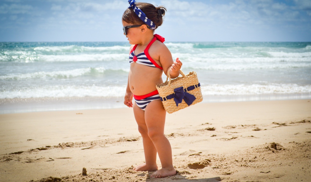 Маленькая девочка в купальнике гуляет по пляжу 