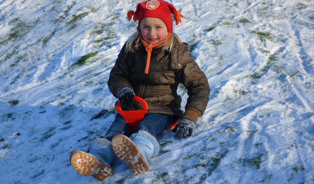 Маленькая девочка катится с горки по снегу