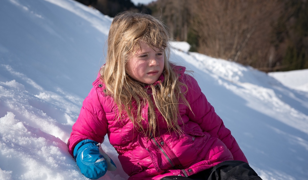 Маленькая девочка лежит на заснеженной горке 