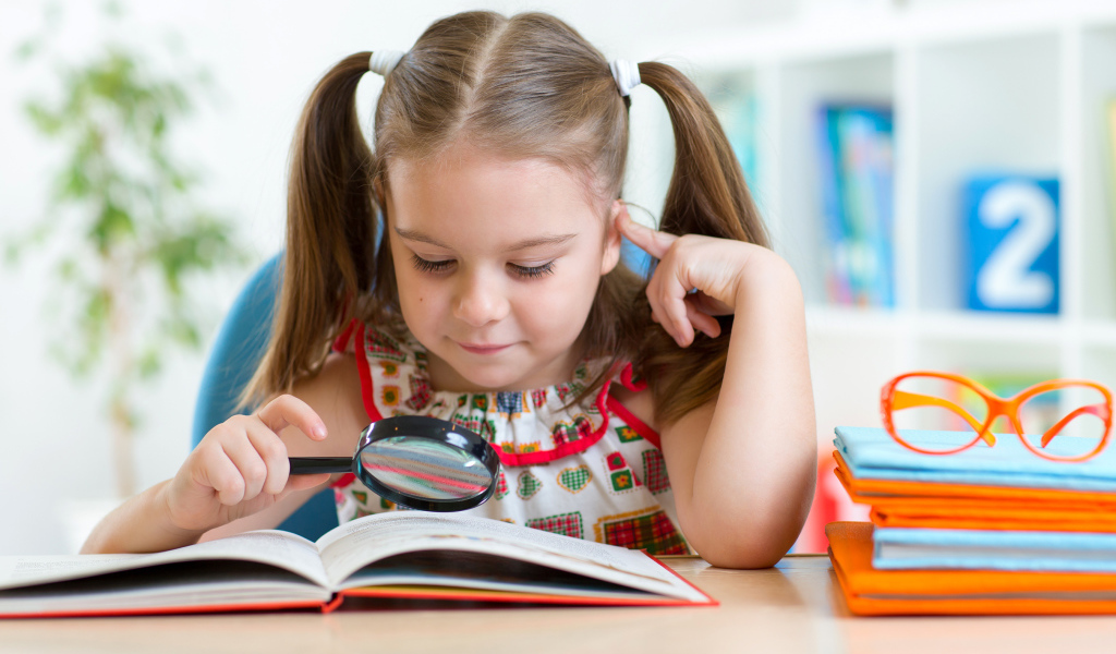 Маленькая девочка читает книгу с увеличительным стеклом 