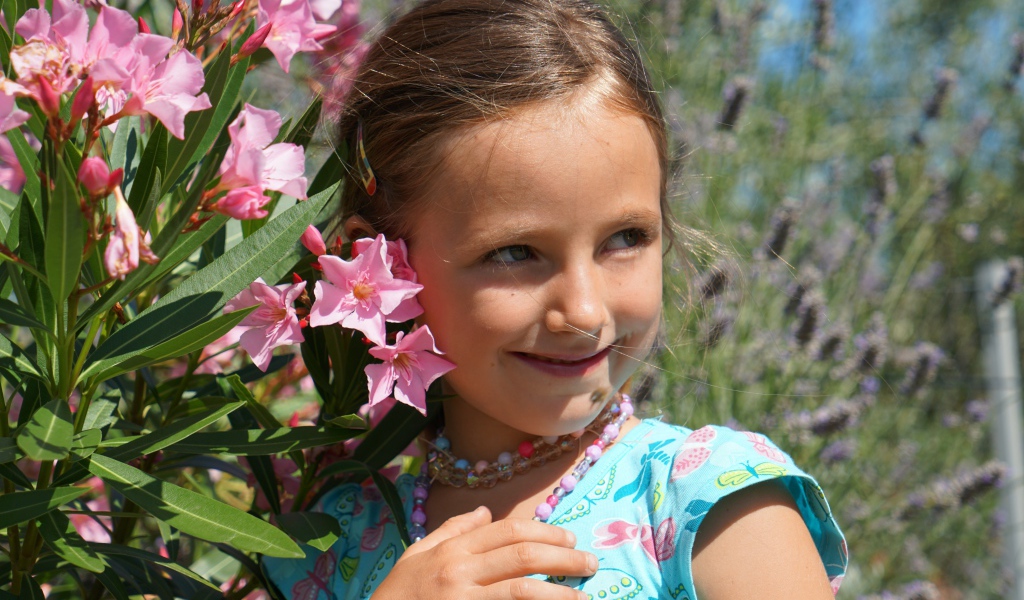 Маленькая девочка стоит у растения с розовыми цветами 