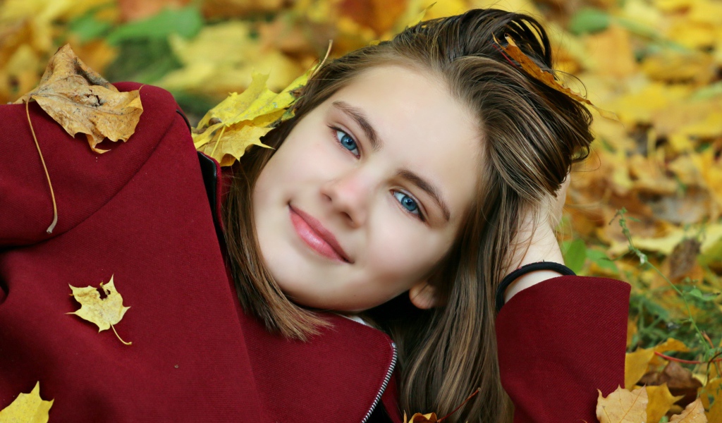 Красивая голубоглазая девочка лежит на опавшей листве