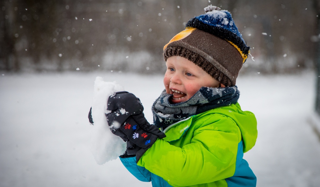 Веселый маленький мальчик со снегом в руках 
