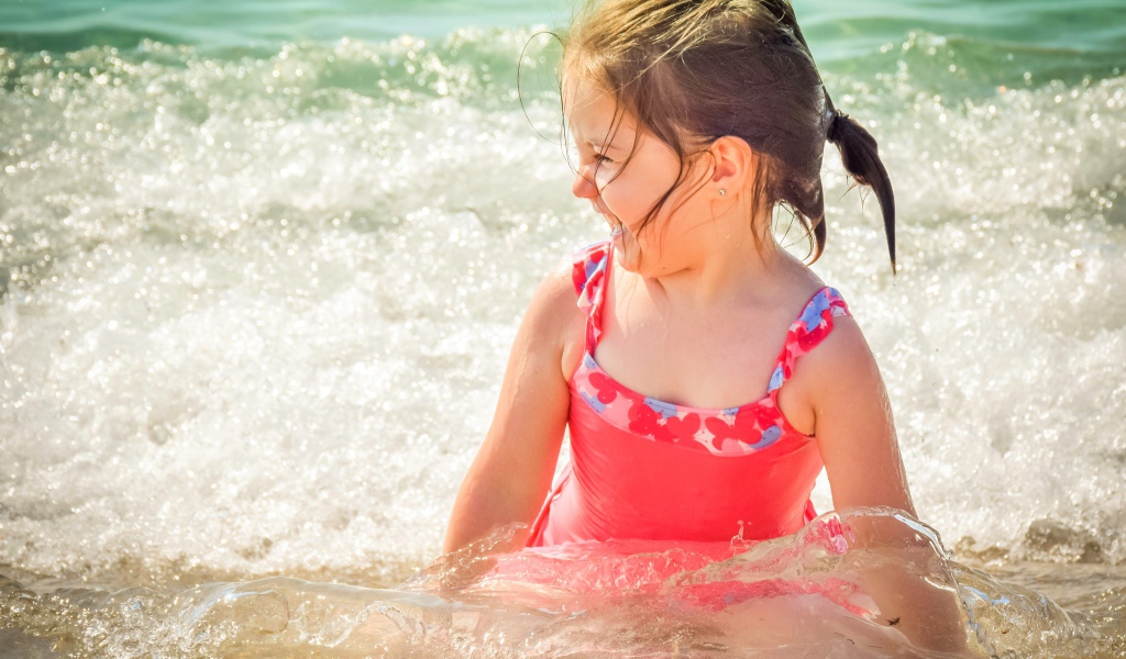 Веселая маленькая девочка в купальнике сидит в воде 