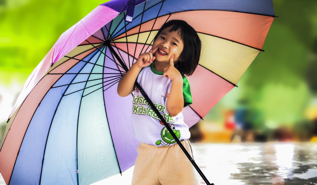Маленькая девочка азиатка под большим разноцветным зонтом 