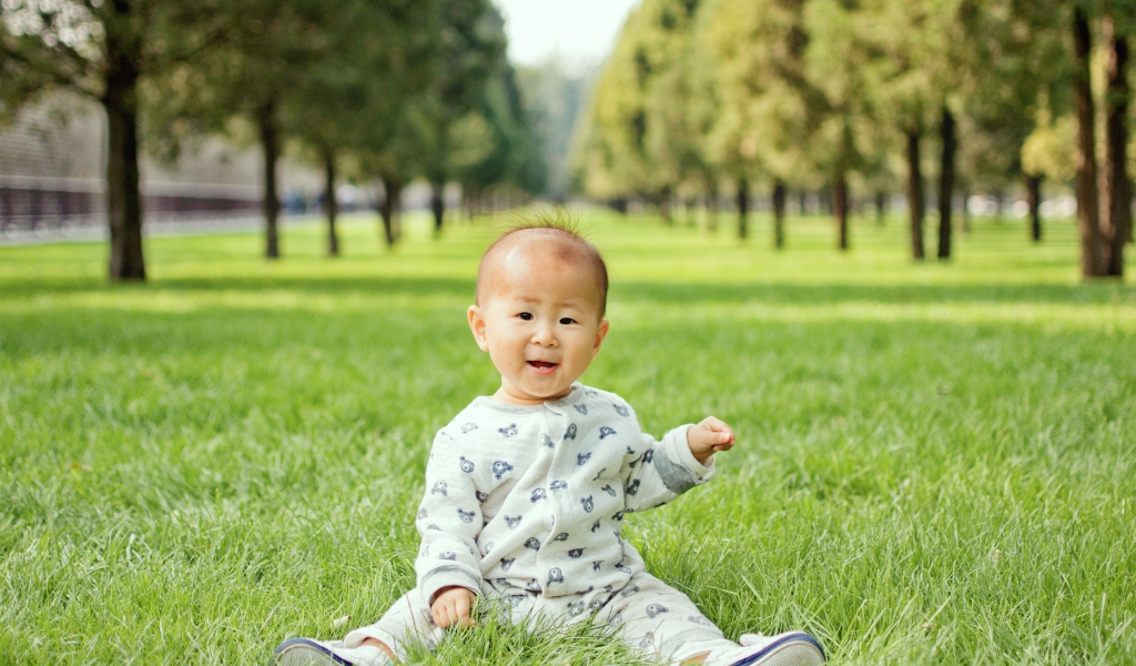 Маленький ребенок азиат сидит на зеленой траве 