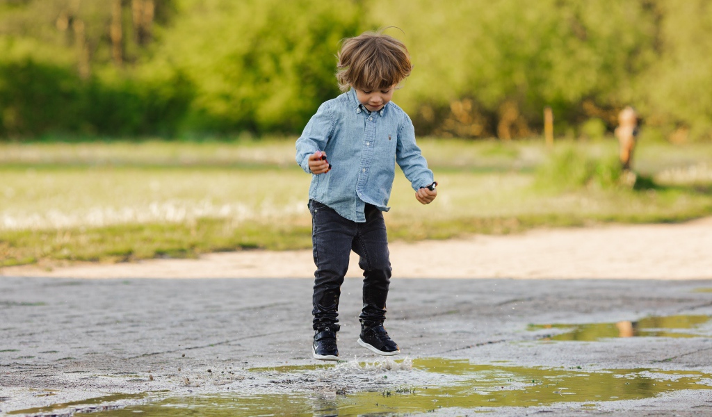 Маленький мальчик прыгает по лужам