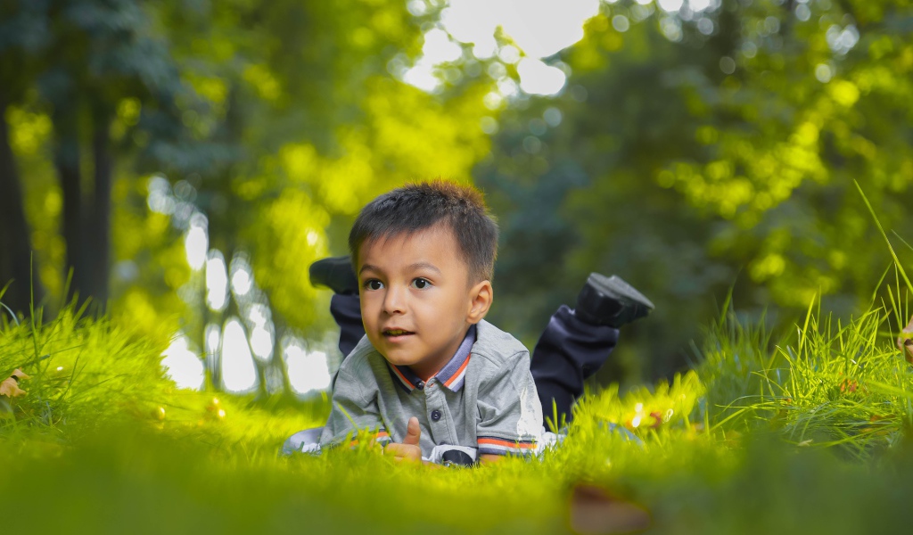 Маленький мальчик лежит на зеленой траве 