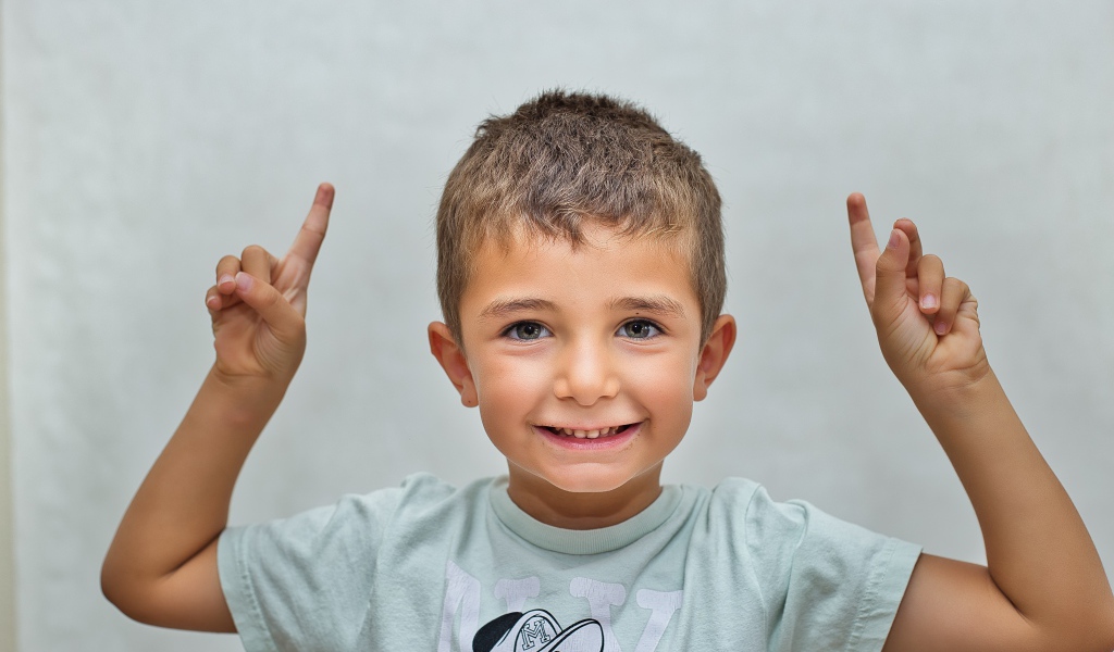 Маленький мальчик поднял руки вверх на сером фоне