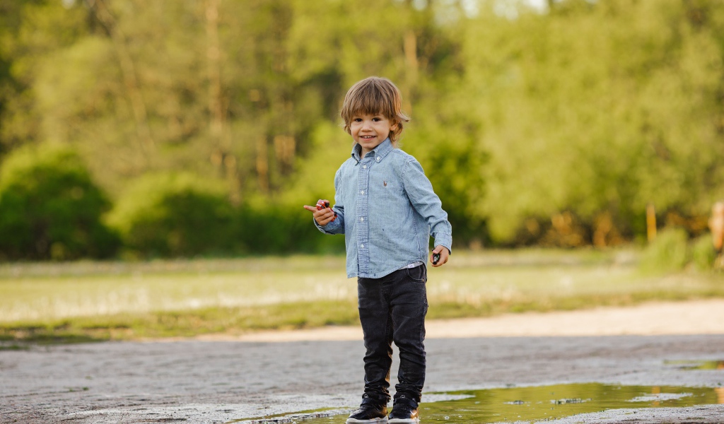 Маленький мальчик стоит в луже на дороге 