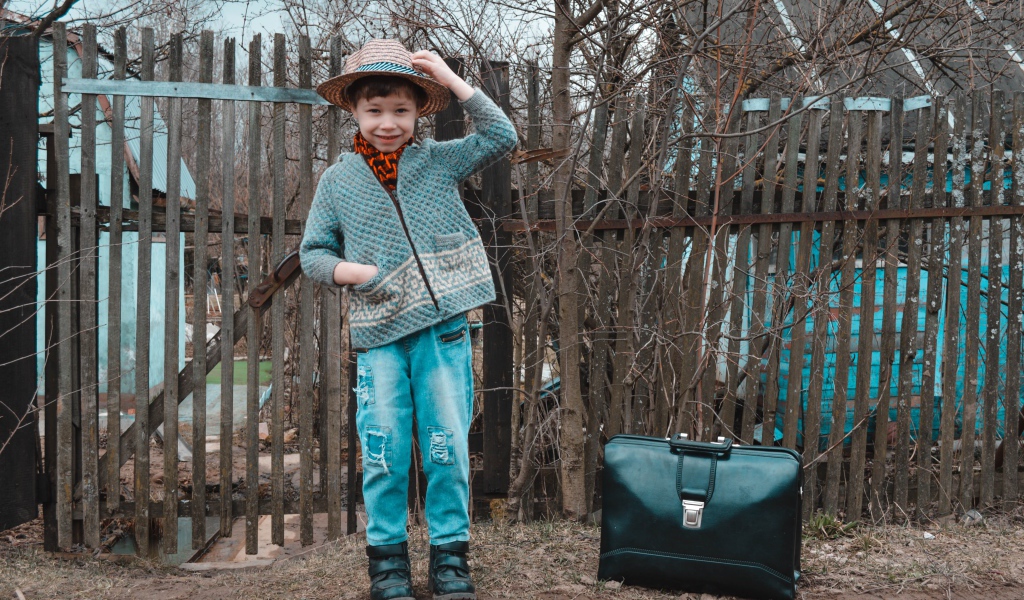 Маленький мальчик с чемоданом у забора