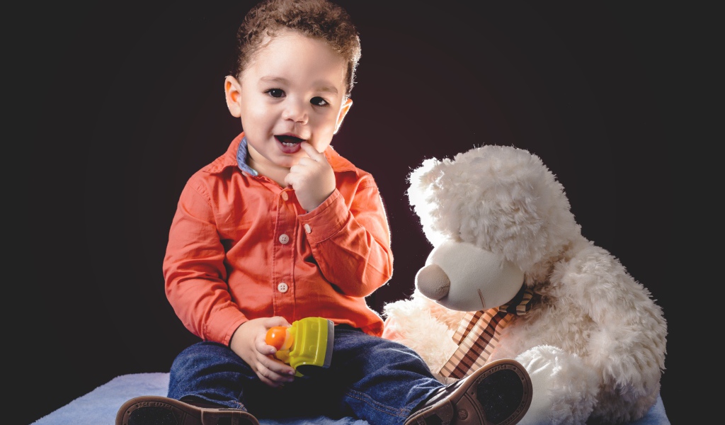 Маленький мальчик с игрушечным медведем на черном фоне