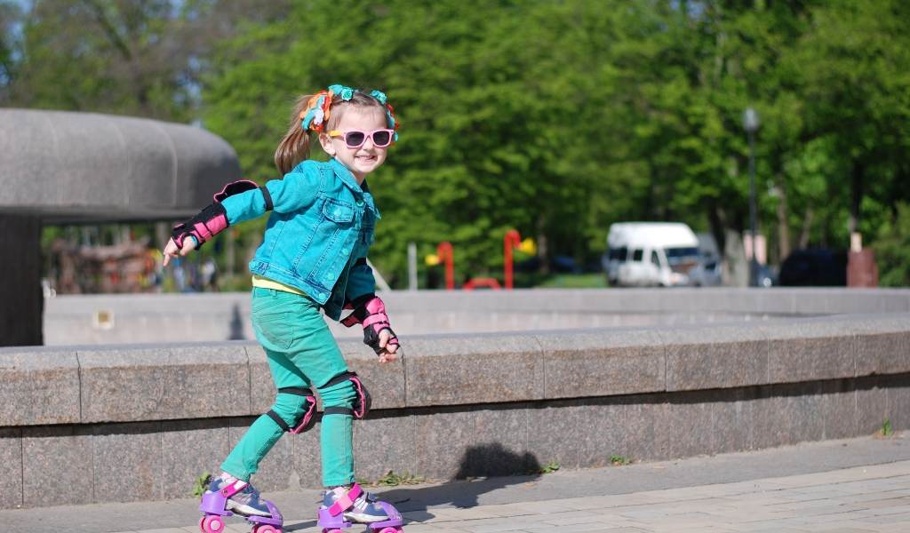Маленькая веселая девочка катается на роликах