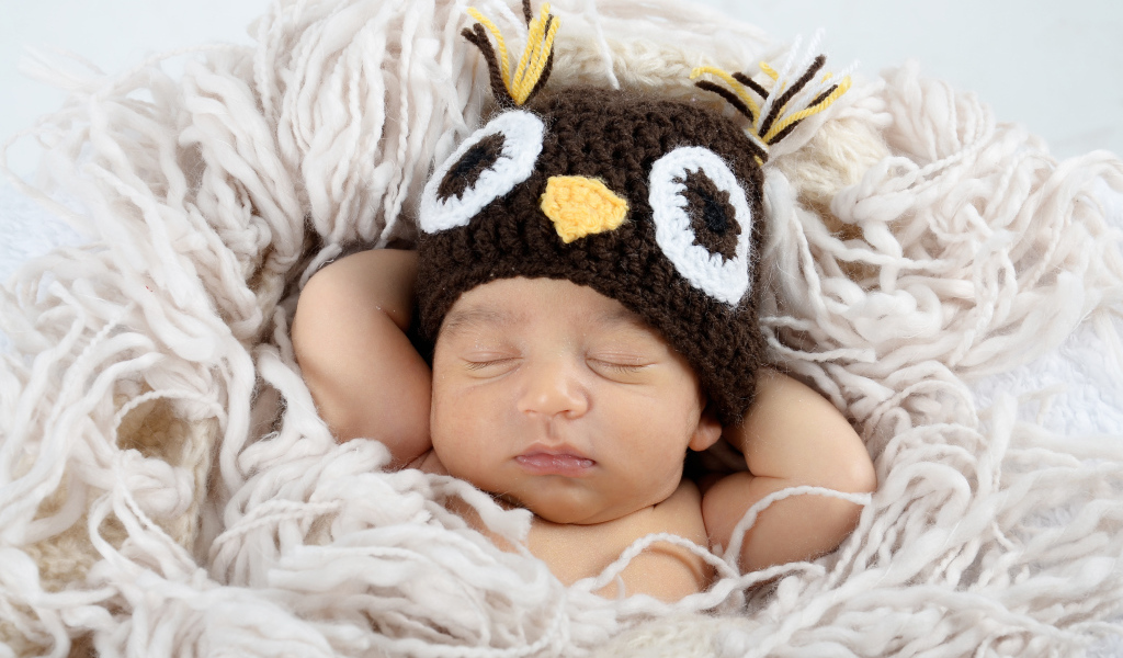 Маленький ребенок  в вязаной шапке спит на кровати 