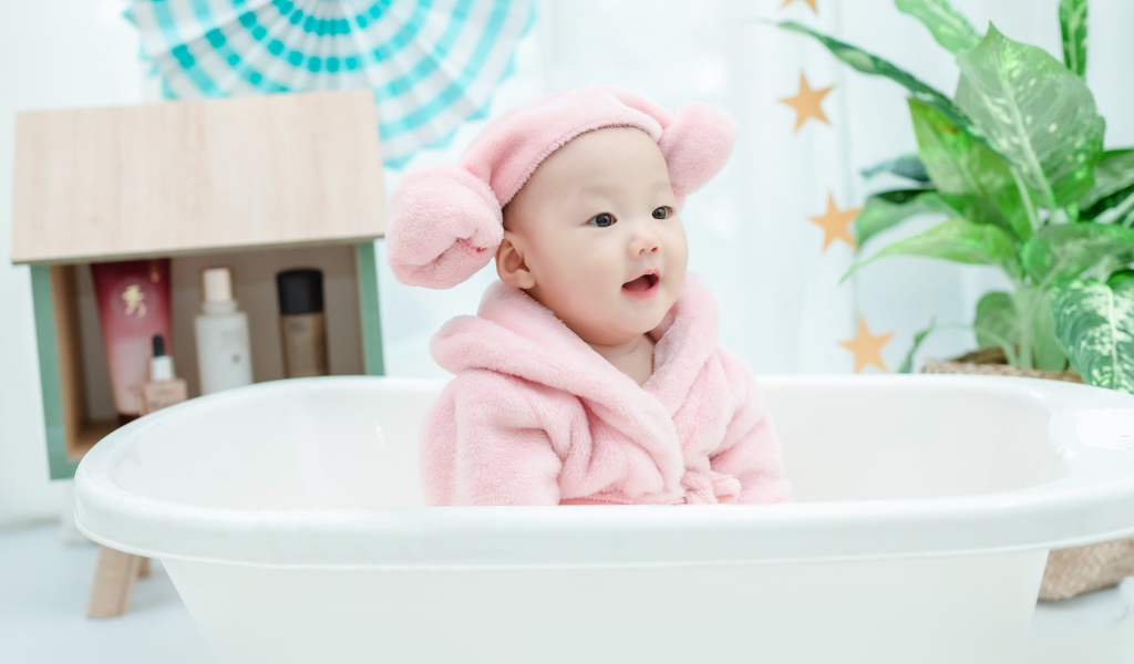Маленький ребенок в розовом халате сидит в белой ванной