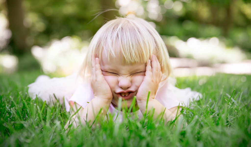 Маленькая смешная девочка лежит на зеленой траве 