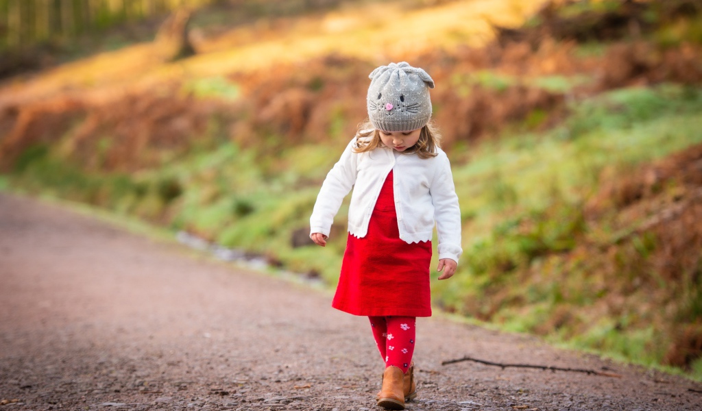 Маленькая девочка в красном платье идет по дороге 