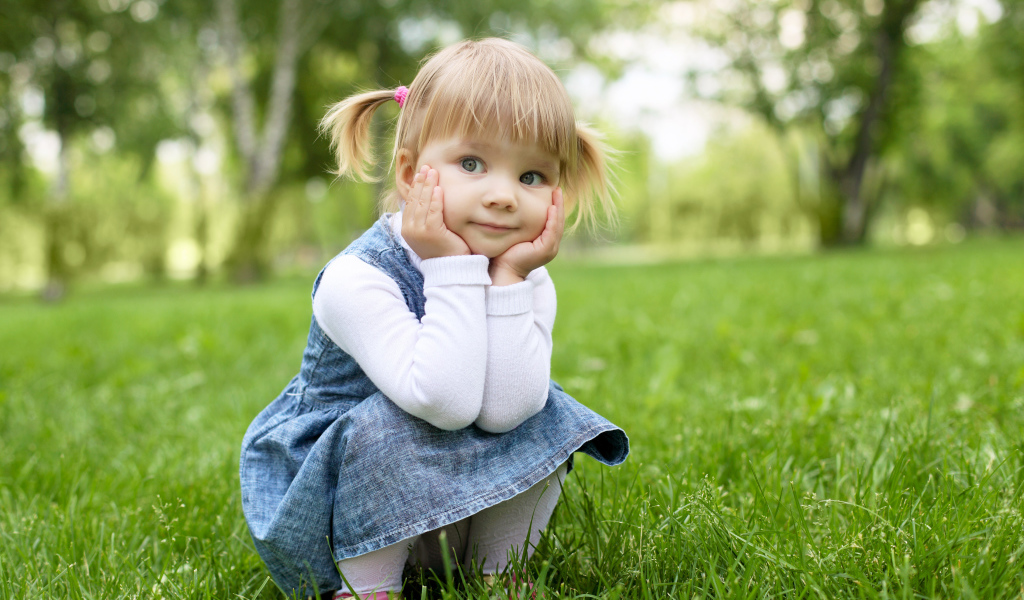 Маленькая девочка в сарафане сидит на траве 