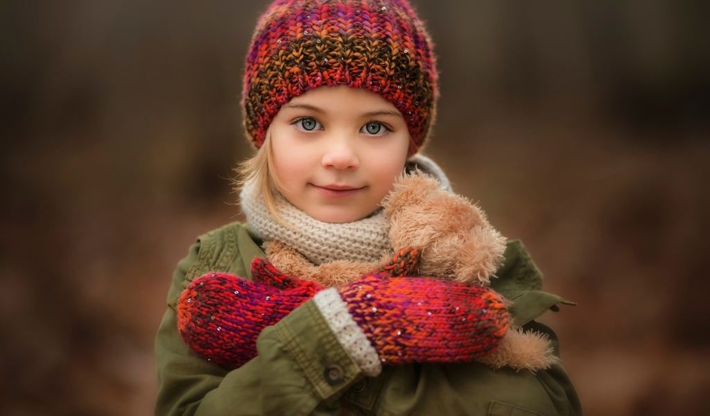 Маленькая девочка в теплой шапке и варежках  с игрушкой в руках 