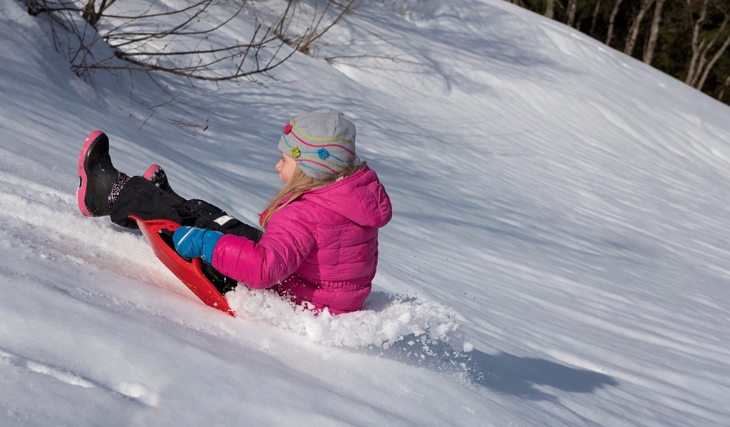 Маленькая девочка катится с заснеженной горки 