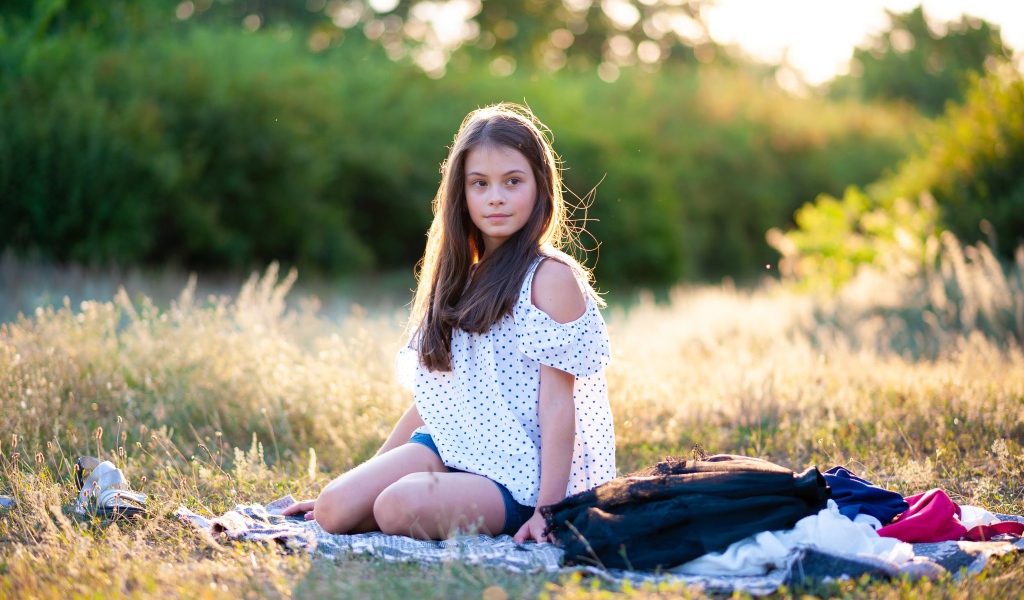 Маленькая девочка сидит на покрывале на земле 