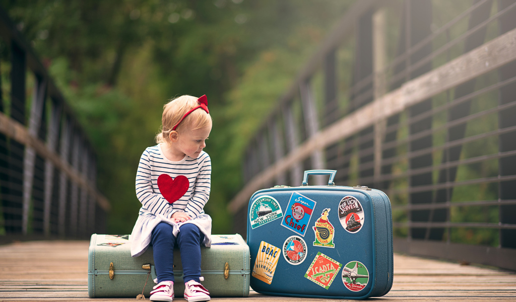 Маленькая девочка сидит на мосту с чемоданами