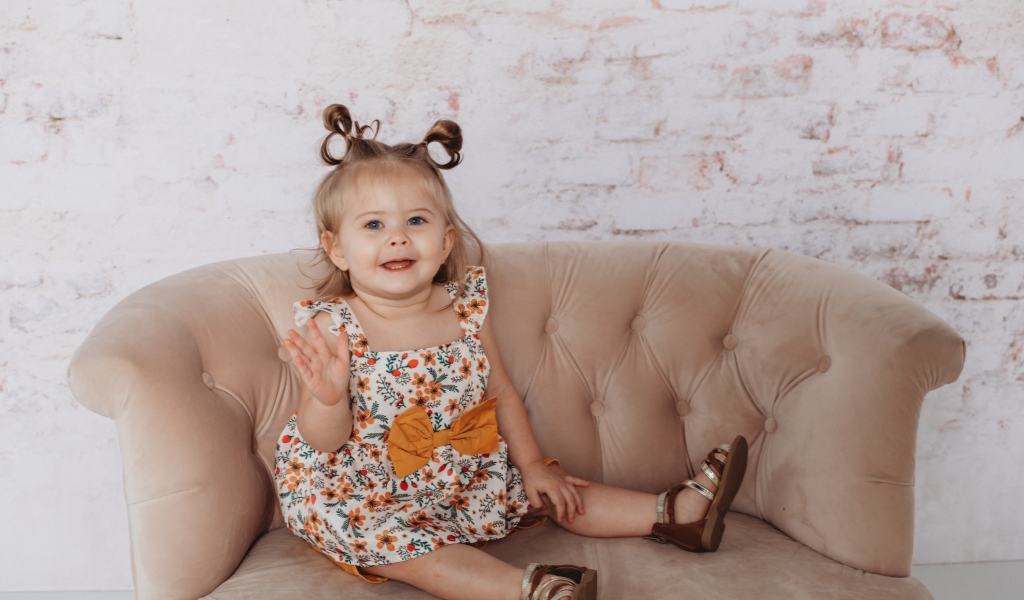 Маленькая девочка сидит на диване у стены