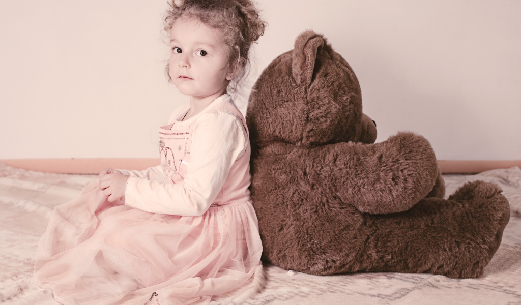 Маленькая девочка сидит с большим медведем