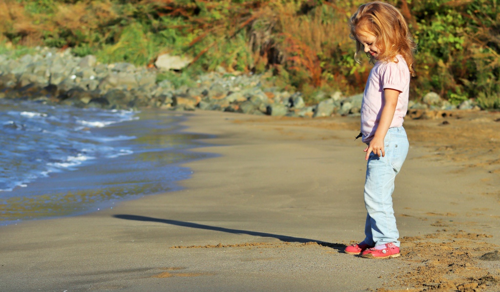 Маленькая девочка гуляет по мокрому песку 