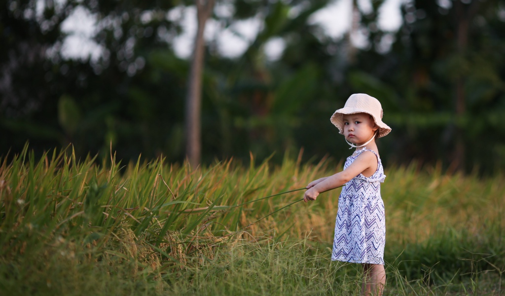 Маленькая девочка с панамой на голове  стоит в траве