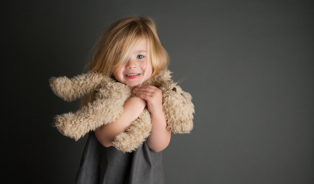 Маленькая девочка с игрушечным медвежонком в руках  на сером фоне 