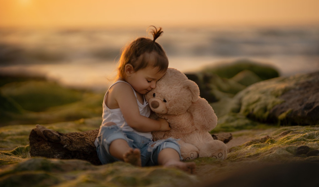 Маленькая девочка с игрушечным медведем сидит на камне