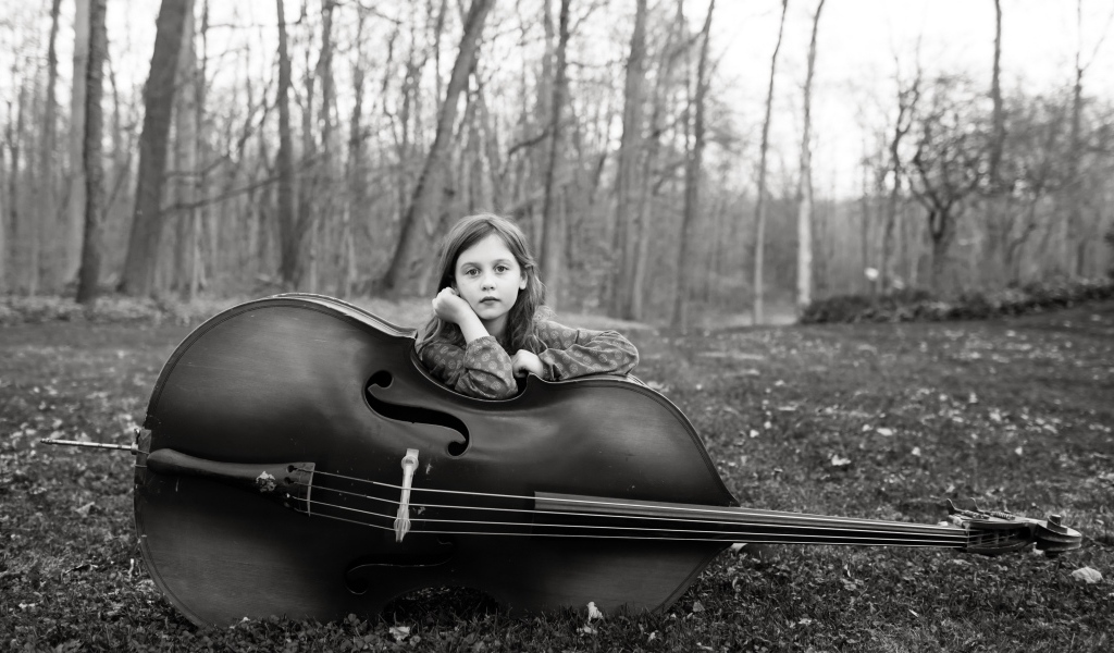 Маленькая девочка с виолончелью сидит в парке