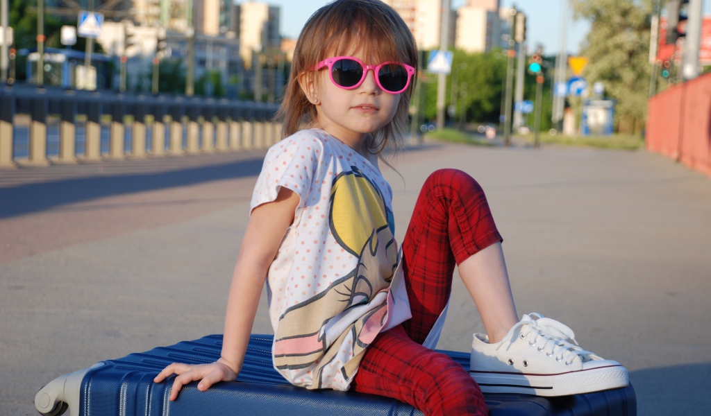 Маленькая девочка в очках сидит на чемодане