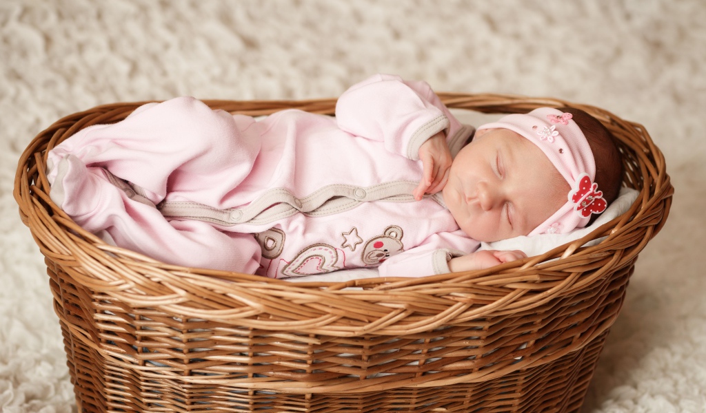 Маленькая новорожденная девочка в розовом костюме спит в корзине 
