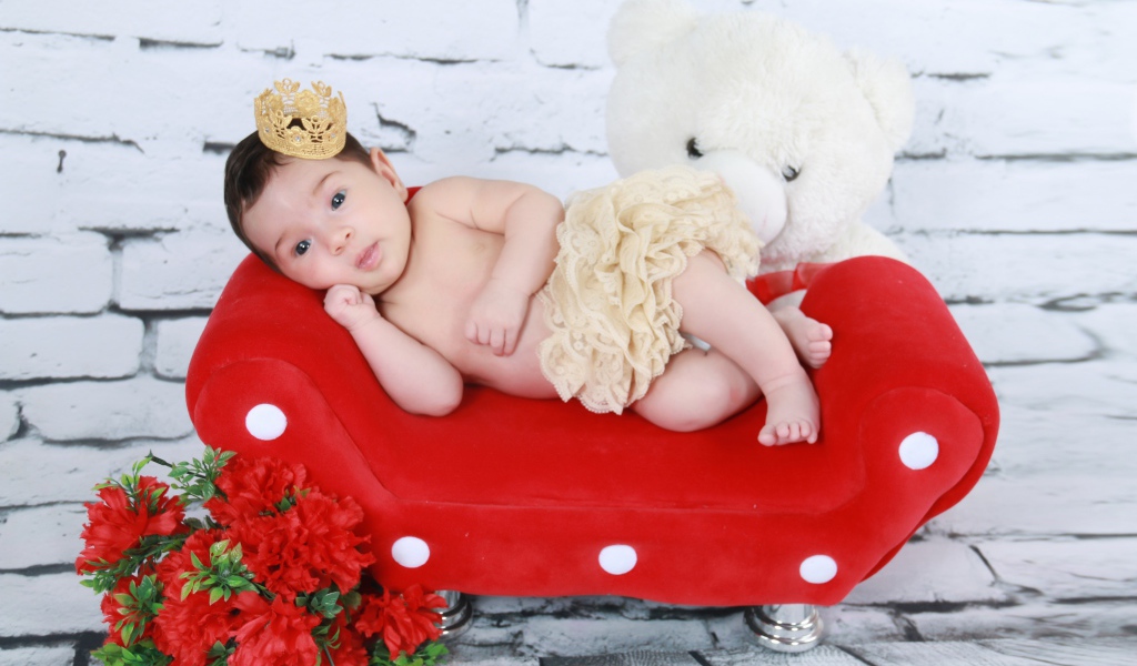 Маленькая принцесса лежит на красном диване у стены 