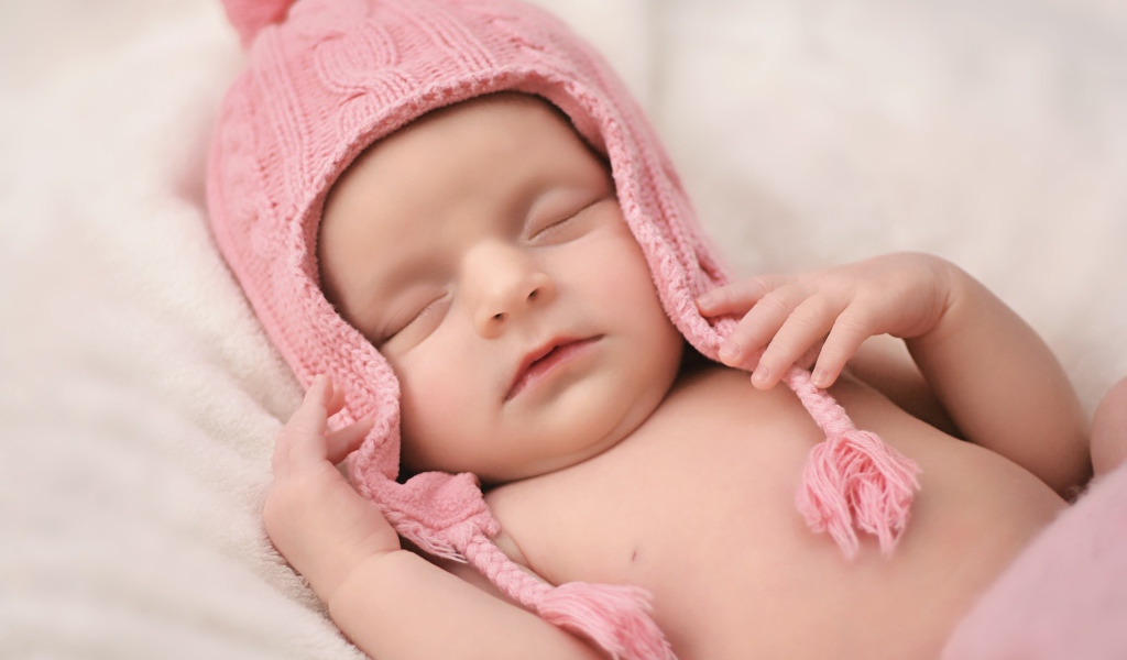 Маленький спящий ребенок в розовой вязаной шапке 