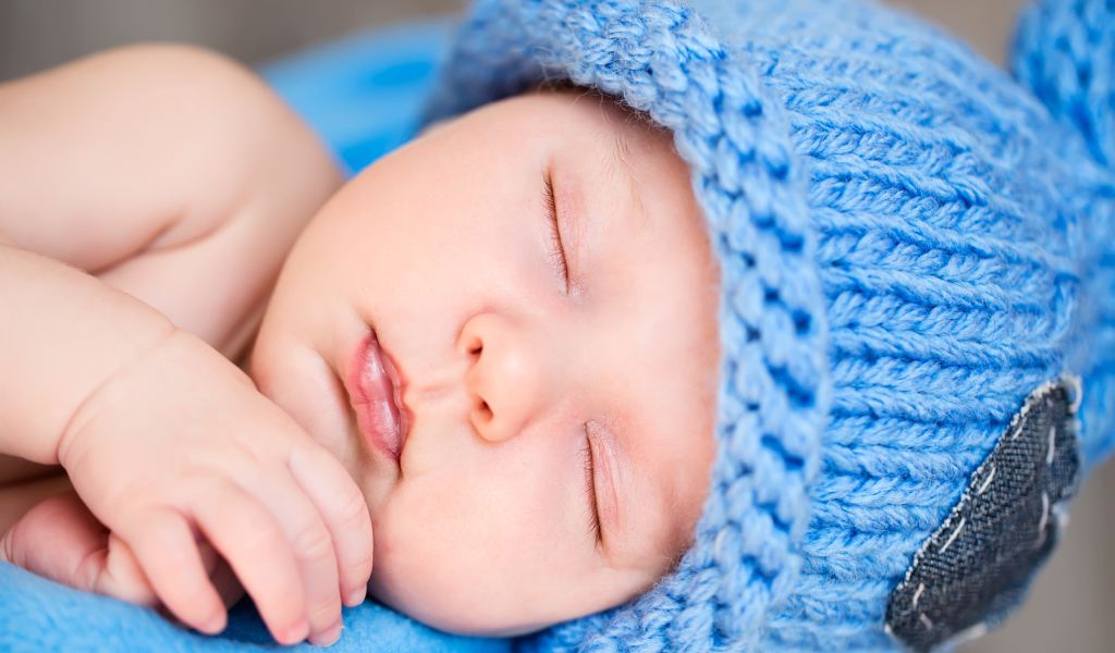 Маленький спящий грудной ребенок в голубой вязаной шапке 